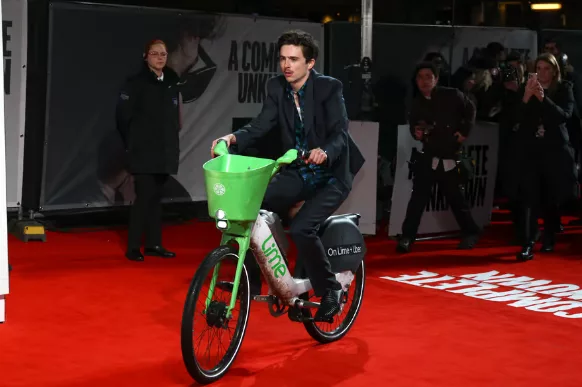 Timothée Chalamet arriving on a Lime bike at the A Complete Unknown premiere red carpet.