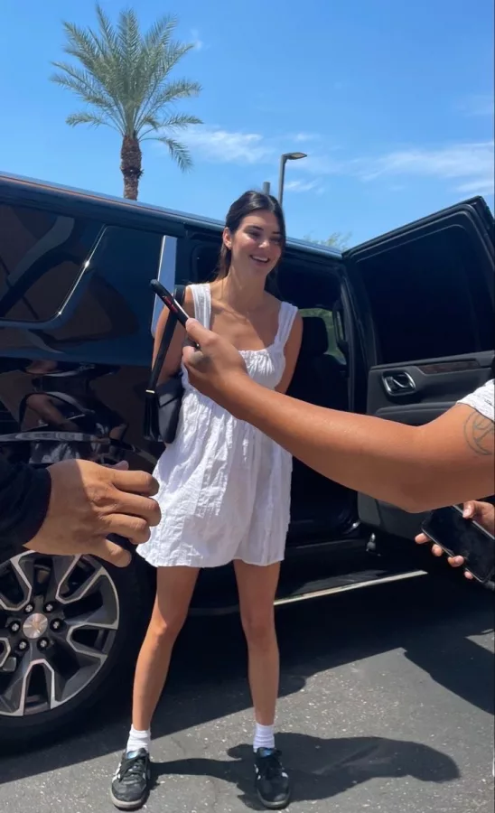 Kendall Jenner pairing Adidas Samba sneakers with a simple white dress and a black leather shoulder bag for a minimalist style.