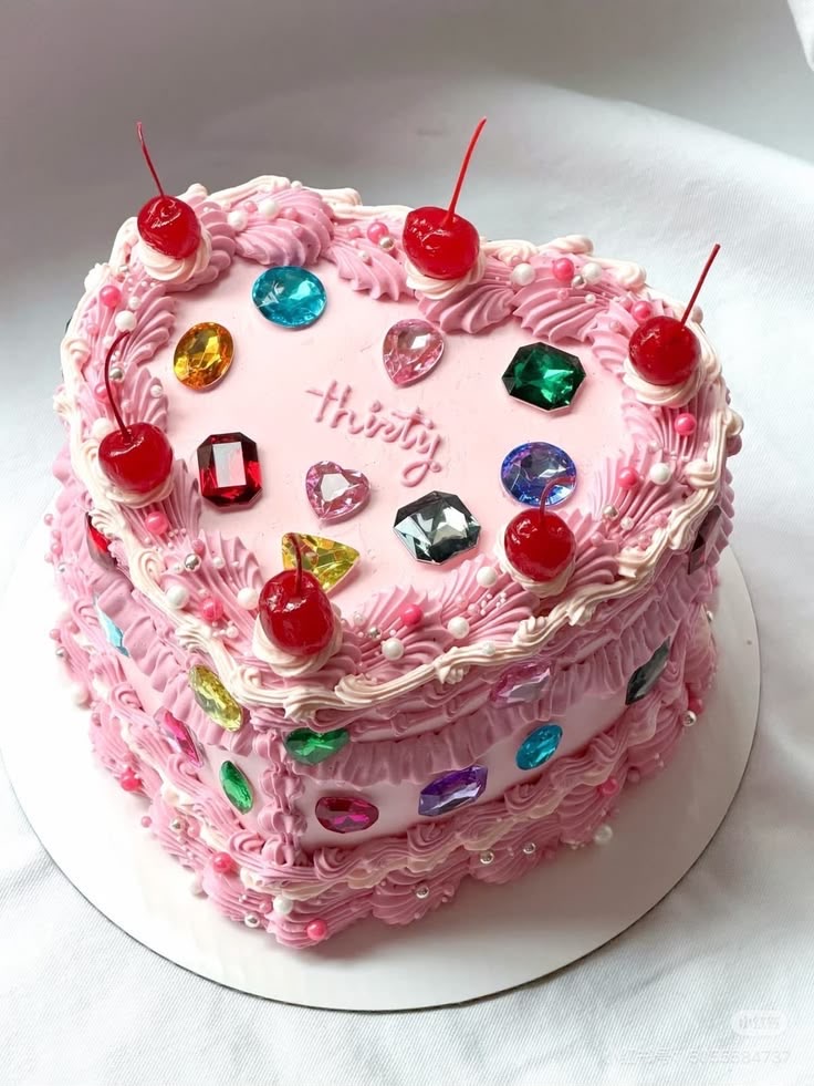Pink heart-shaped cake decorated with colourful gems and cherries