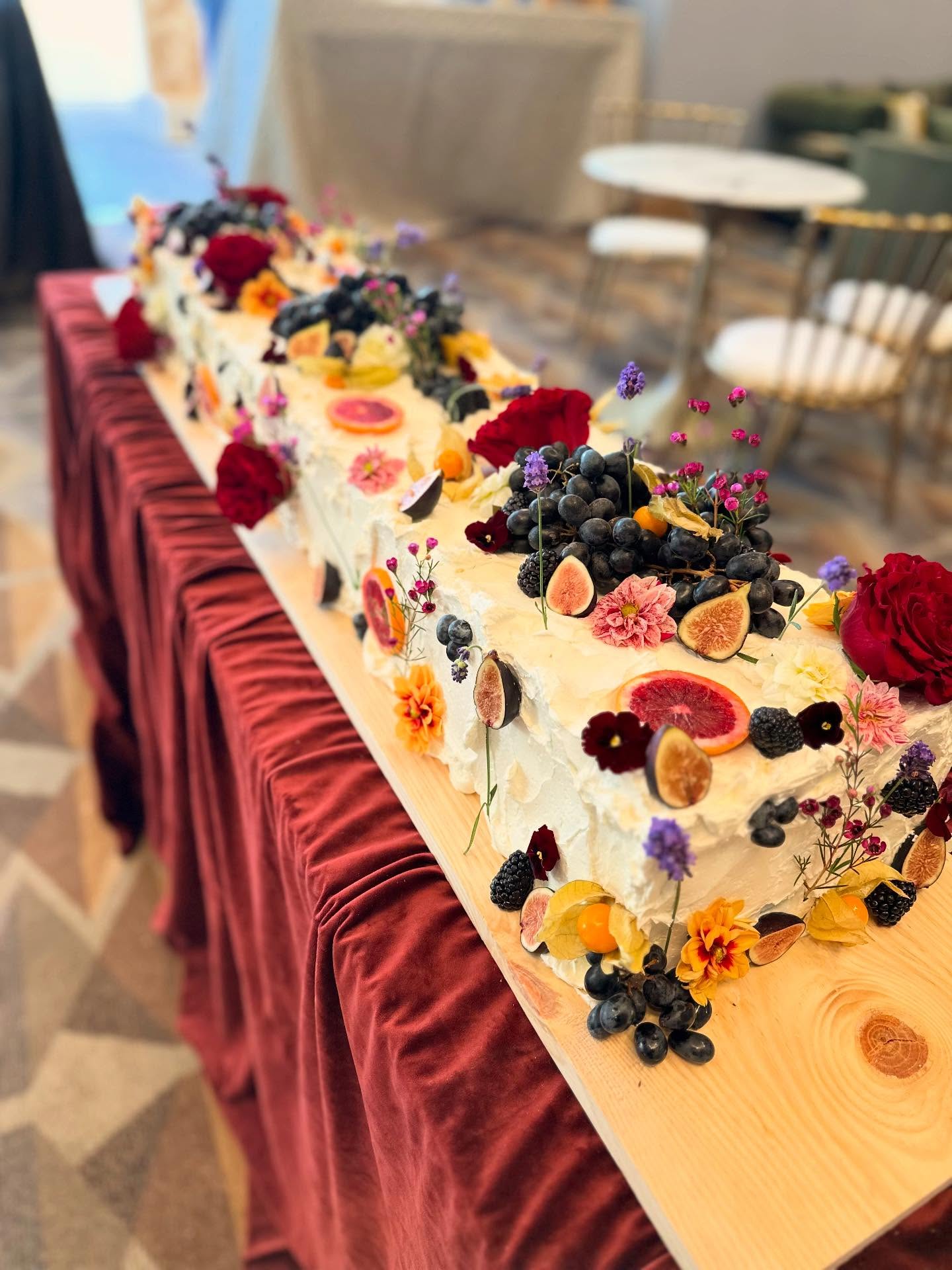 Long rectangular celebration cake decorated with flowers, fruit and piping