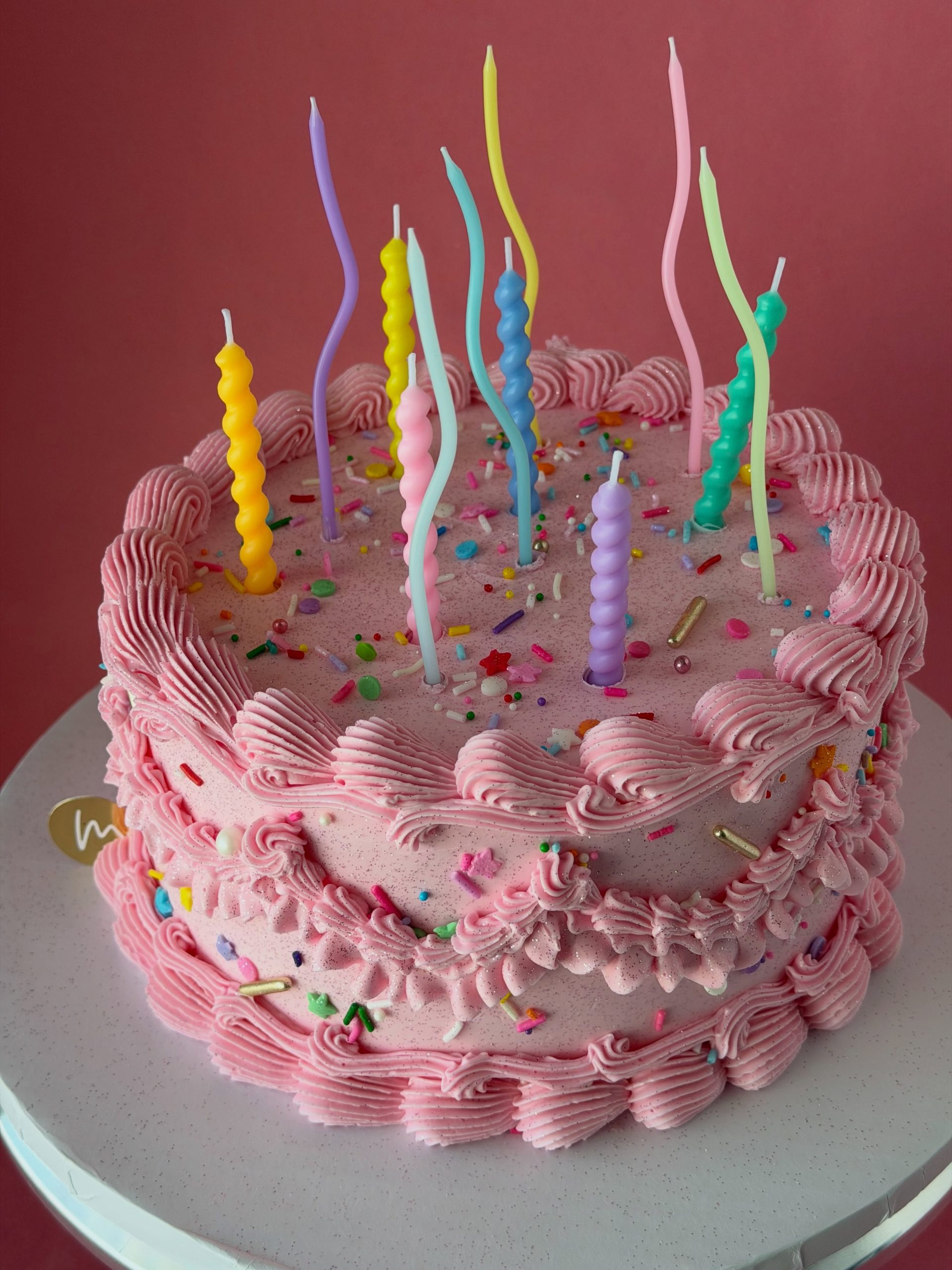 Pink confetti cake decorated with colourful sprinkles and piped borders