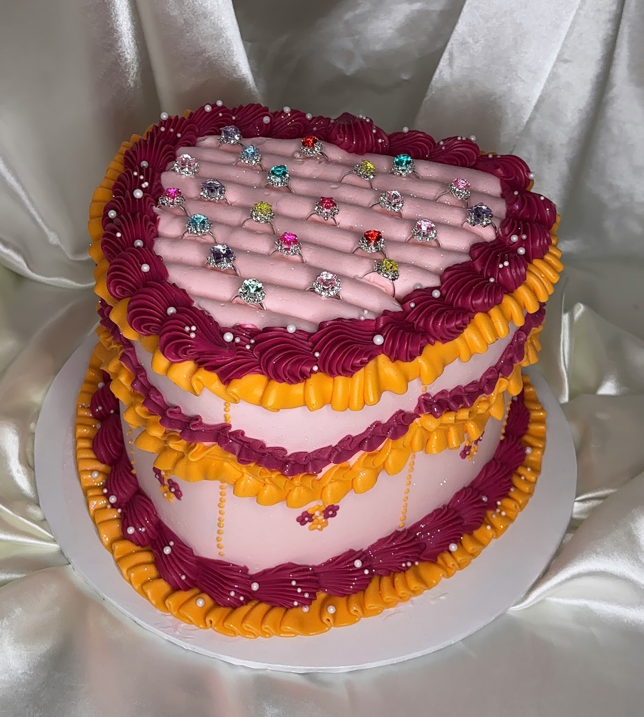 Pink jewellery box cake with rows of colourful jewel rings and ornate piping