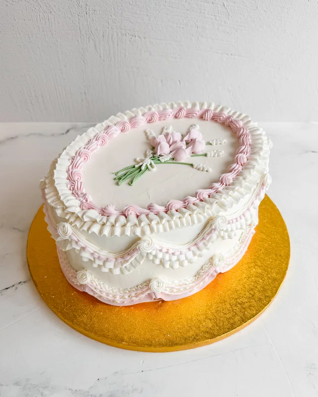 Oval celebration cake decorated with pink and white vintage-style piping