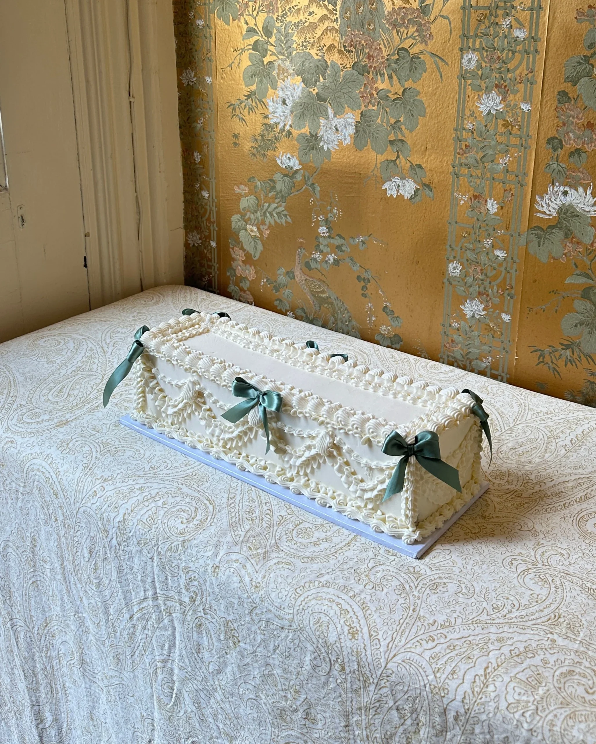 Long rectangular celebration cake decorated with vintage-style piping and green bows