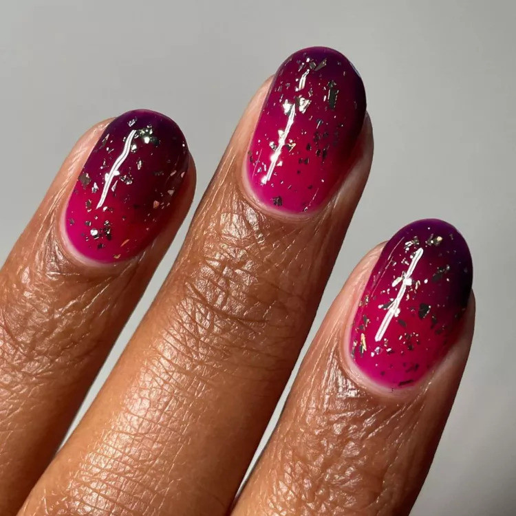 Raspberry jammy nails with a glossy berry finish and scattered metallic detail