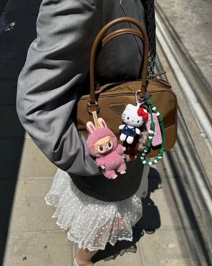 Pink Labubu Toy Fashion Accessory plush with Hello Kitty keychain on a Prada handbag